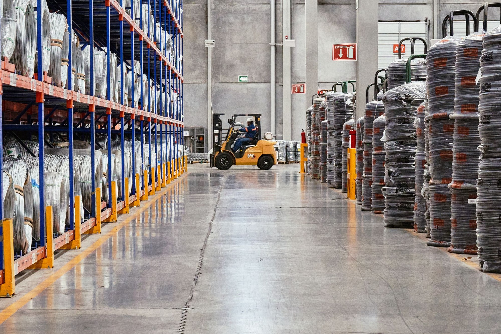 Forklift operator working between racks of coiled wire in a warehouse