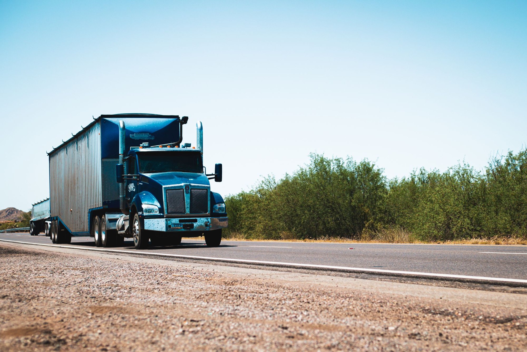 Blue semi truck hauling a silver trailer along a flat highway