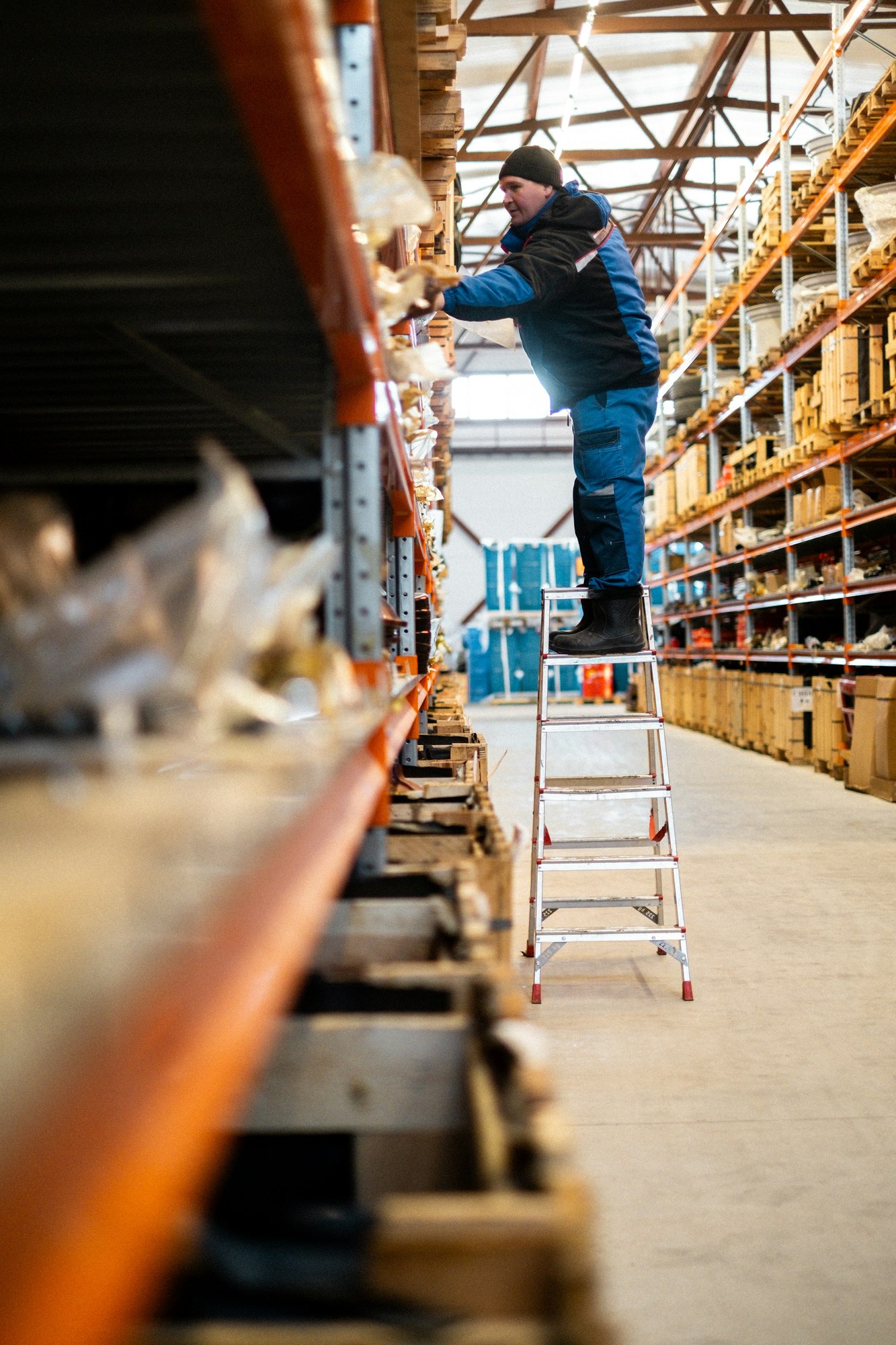 Warehouse worker on a stepladder reaching for goods on a storage rack
